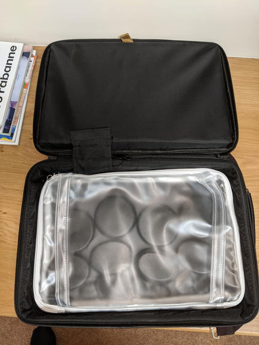 Black travel case with a clear compartment containing round items on a wooden surface.